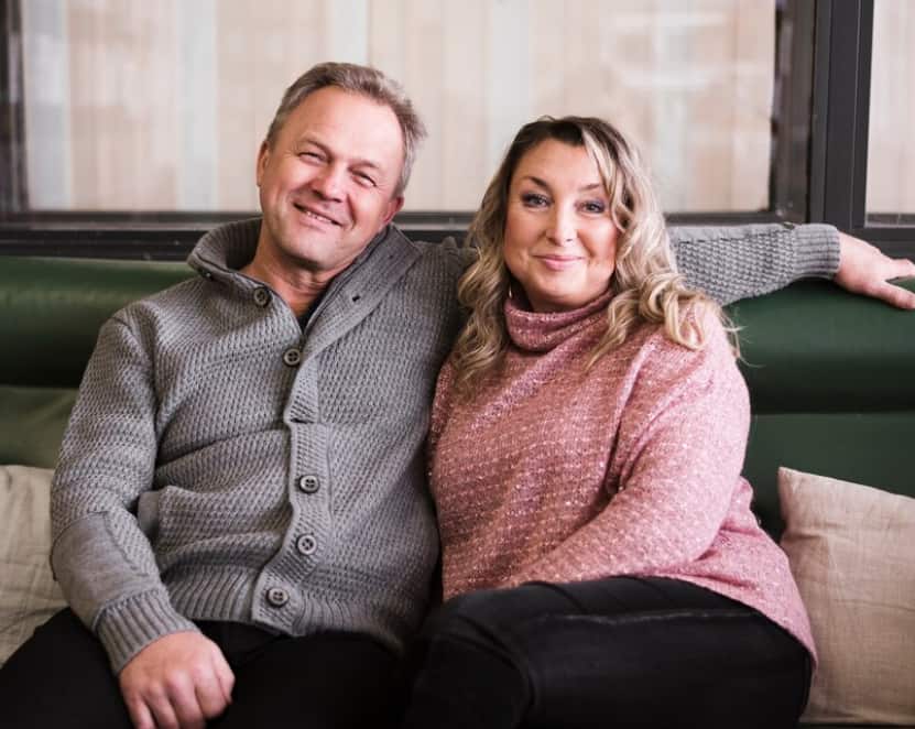 uomo e donna seduti sul divano e sorridenti, l'uomo le tiene la mano sulle spalle